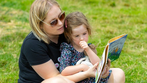 A lady and a young girl reading a story book in the gardens at Hanbury Hall